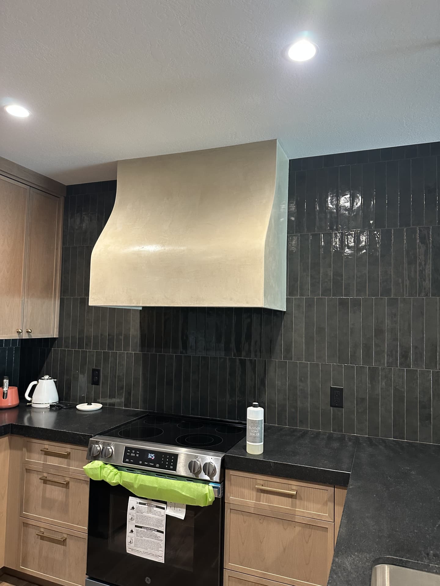 Finished smooth matte beige plaster range hood above a black tile backsplash