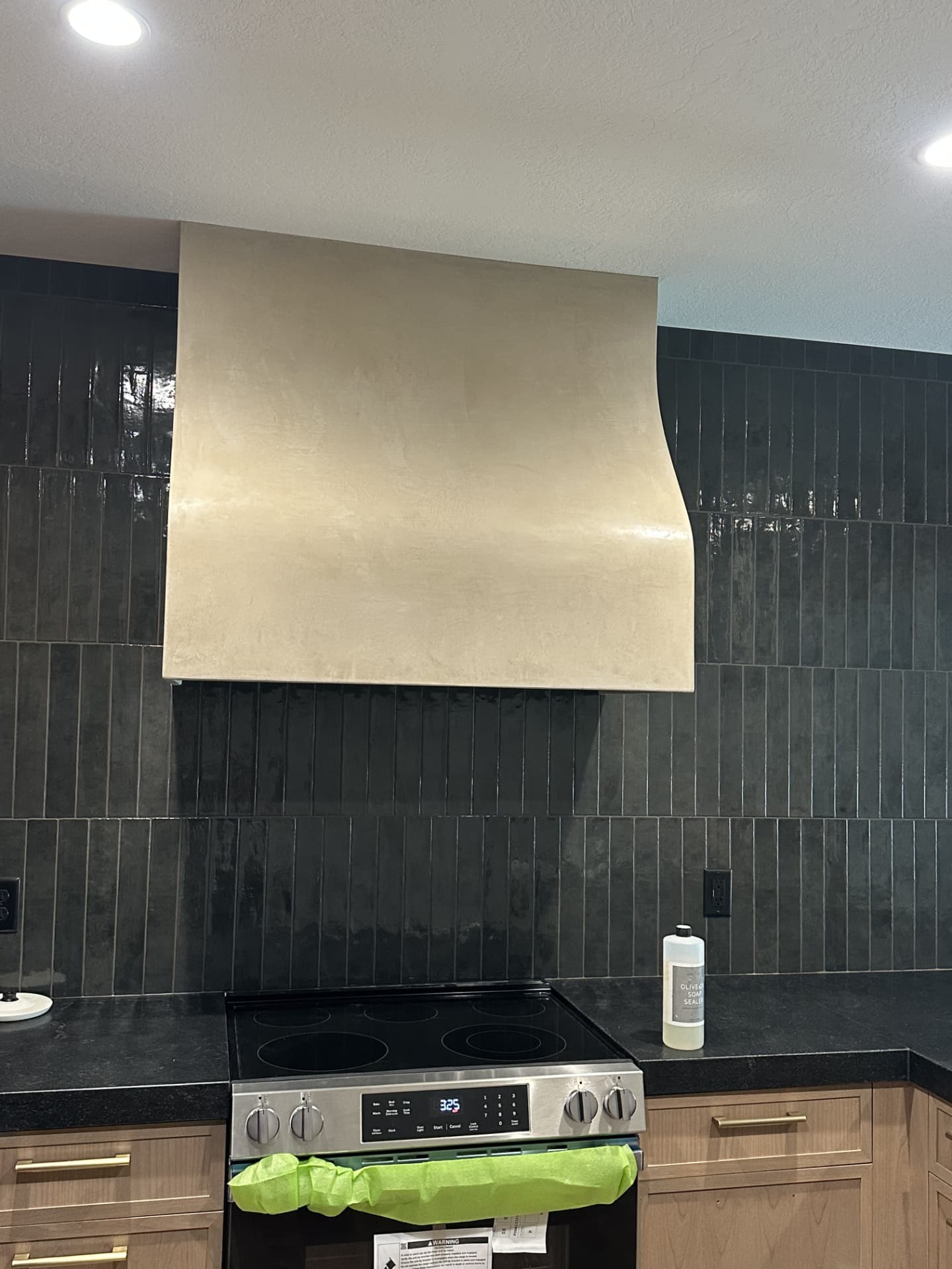 Curved plaster range hood in warm taupe above a stainless stove and light wood cabinets